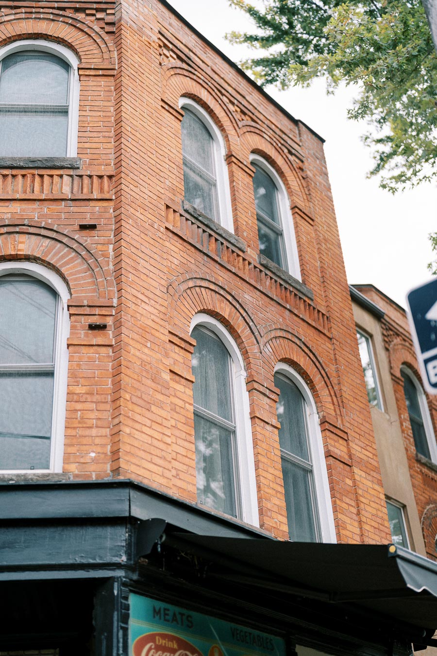 Three-story historic brick building with arched windows, featuring intricate brickwork and a ground-level awning, set against a backdrop of trees.