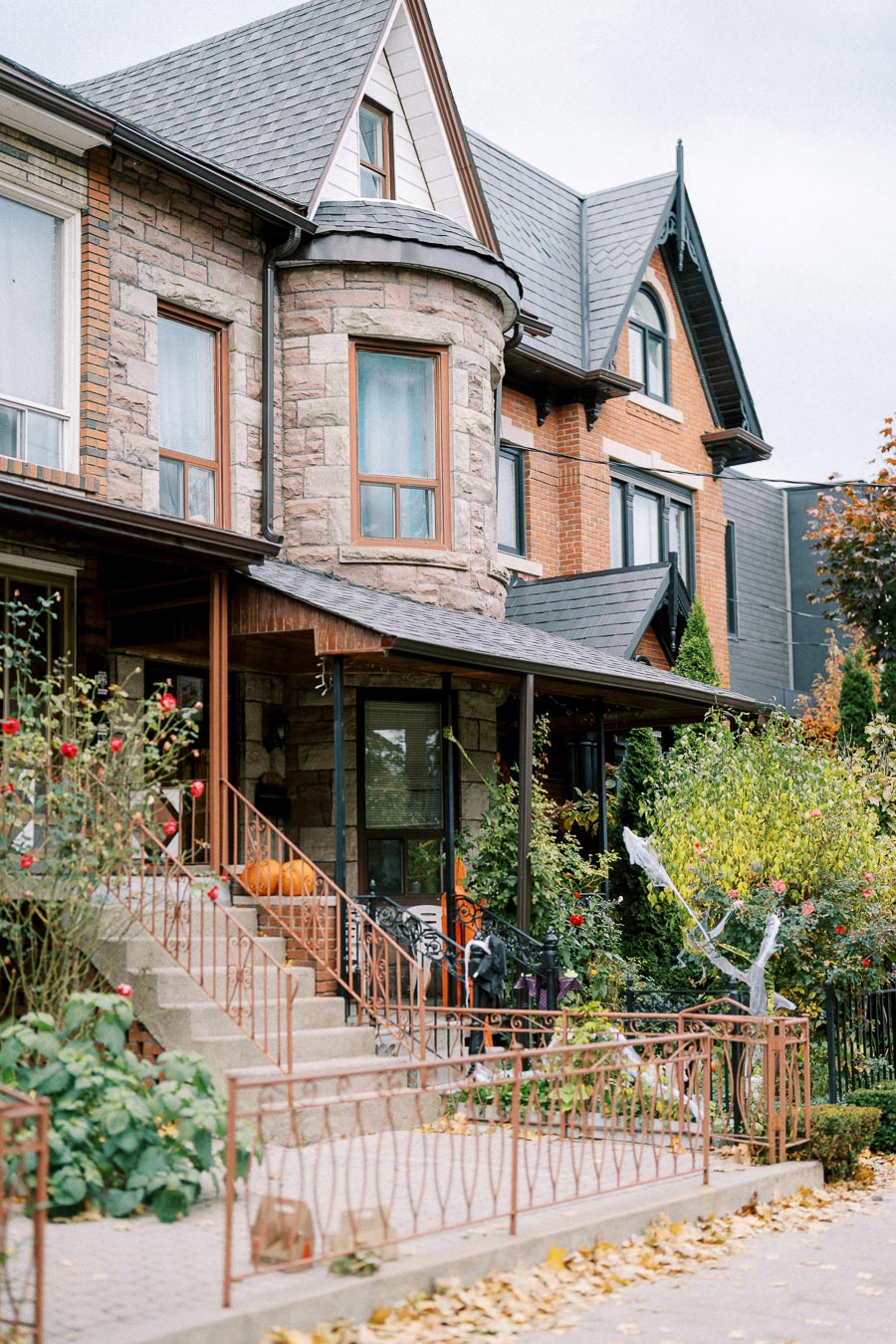 Charming stone and brick townhouse with autumn decorations, including pumpkins on the front porch, surrounded by a garden and trees with fall foliage.
