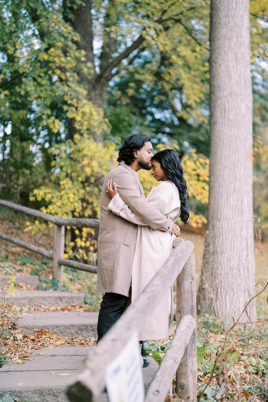 A couple embracing affectionately on a wooded path during autumn, surrounded by colorful fall foliage.