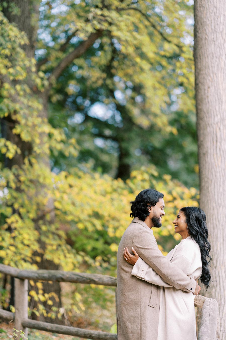A couple embracing in a scenic autumn park, surrounded by vibrant green and yellow foliage.