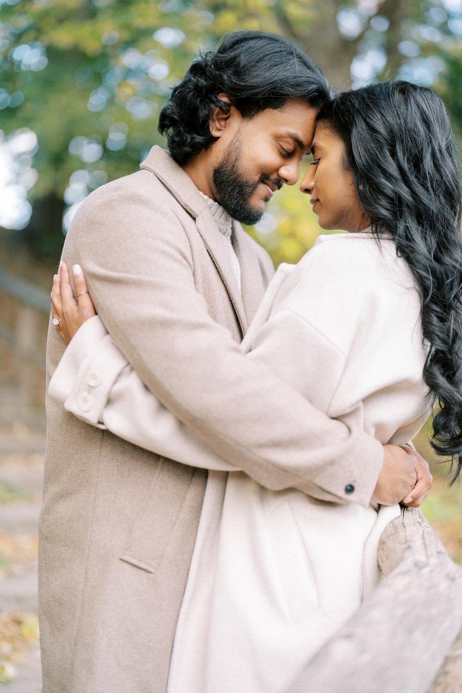 A couple embraces lovingly outdoors in autumn, both wearing beige coats, conveying warmth and romance.
