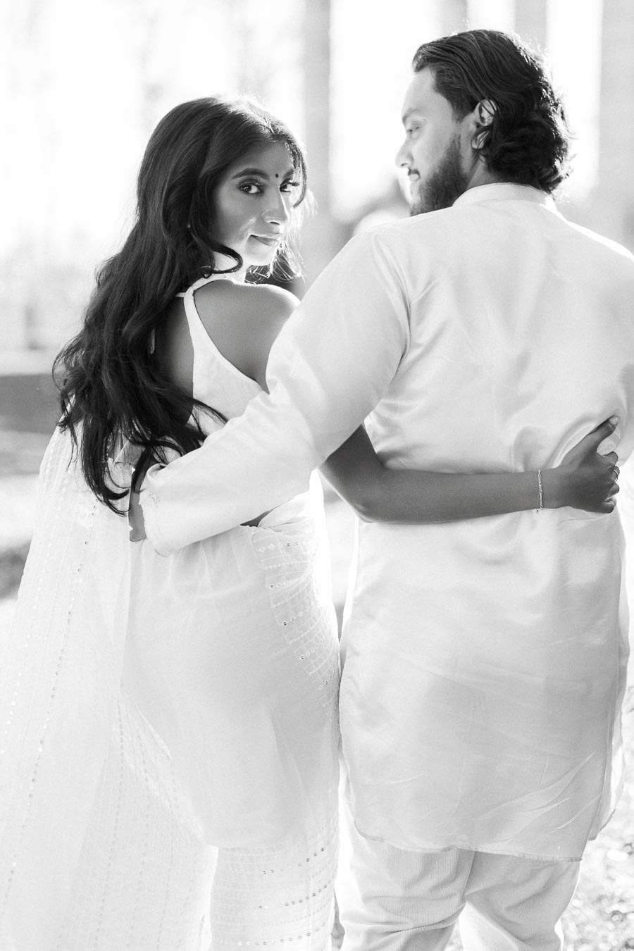 A couple in traditional attire embraces lovingly in a black and white photograph, highlighting their connection and style.