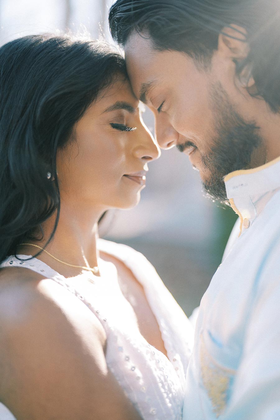 A romantic couple with foreheads touching, eyes closed, and serene expressions, bathed in soft, natural light.