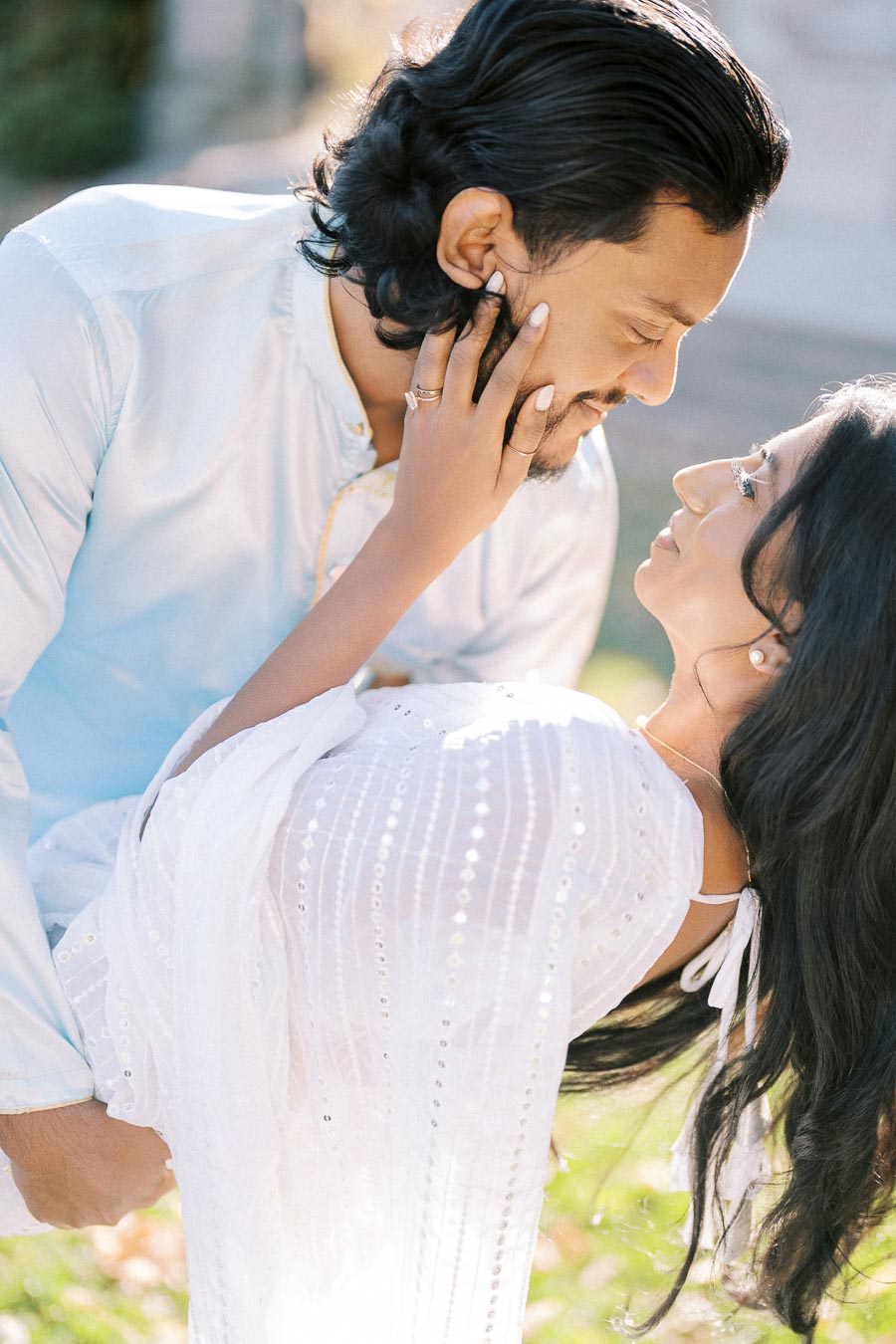 A romantic couple sharing an intimate moment outdoors, with the man gently holding the woman that's leaning back, as they lovingly gaze into each other's eyes, surrounded by soft natural lighting.