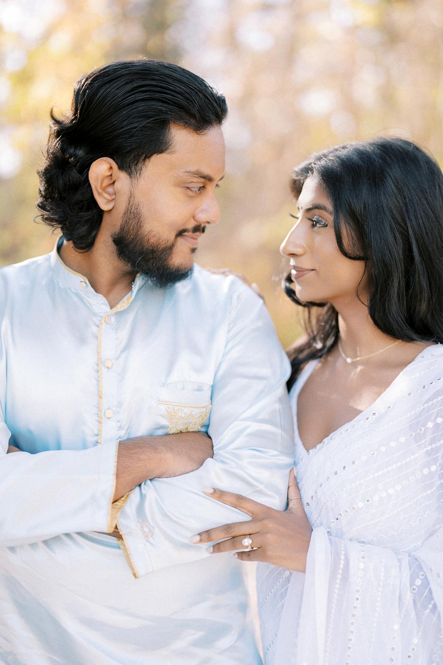 A couple in traditional attire gazing at each other lovingly in a sunlit outdoor setting.