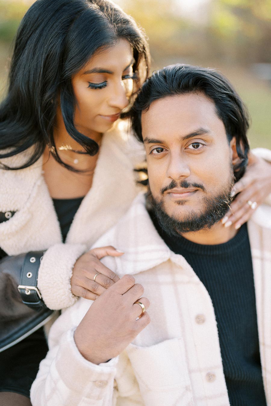 Portrait of a couple outdoors, both wearing cozy jackets and showing affectionate gestures, with a soft focus background and natural lighting highlighting their expressions.