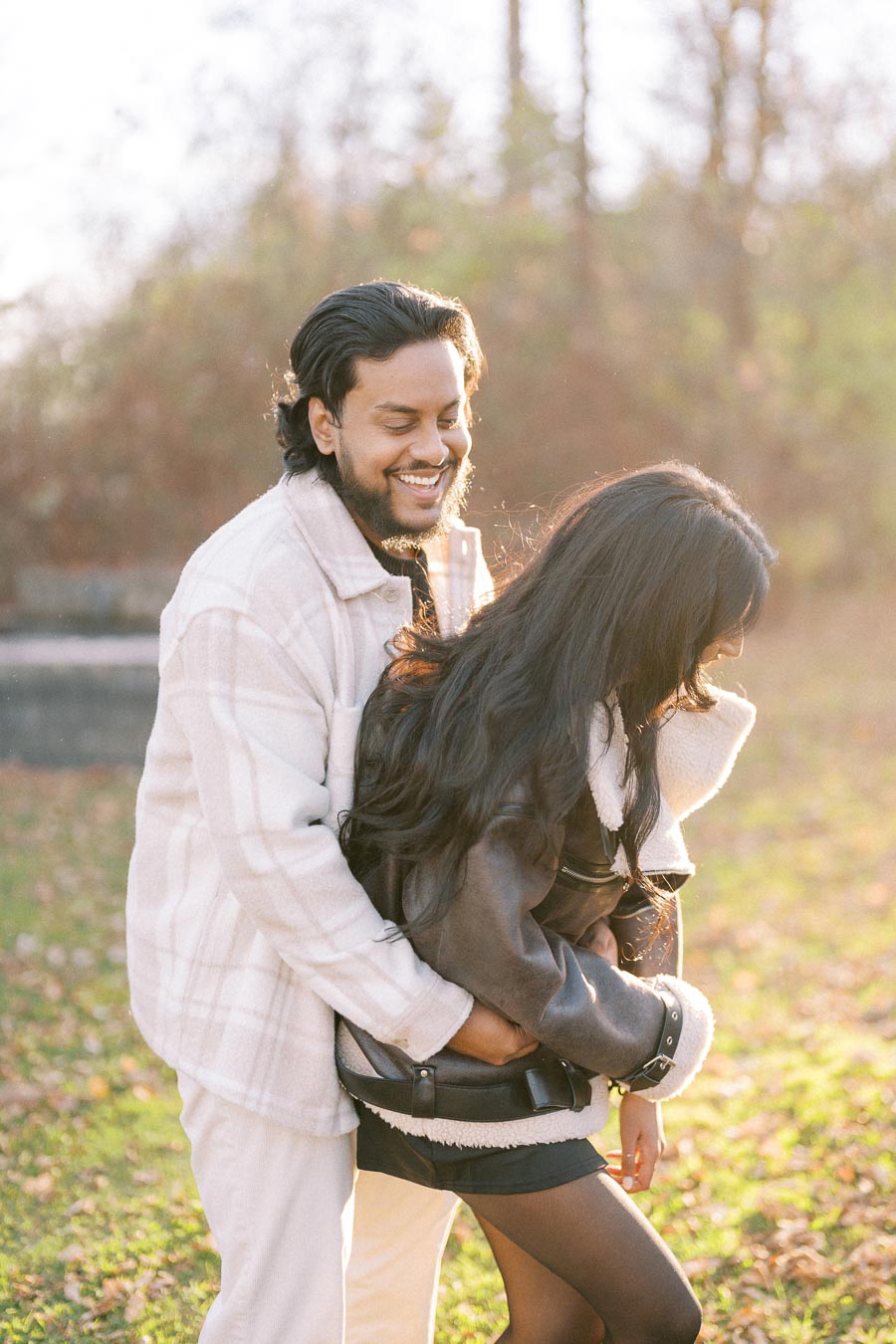 A joyful couple enjoying a sunny autumn day in the park, bundled up in cozy jackets, with fallen leaves covering the ground.