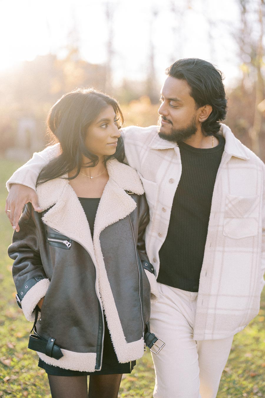 A couple walking together in a sunlit park, wearing stylish winter coats.