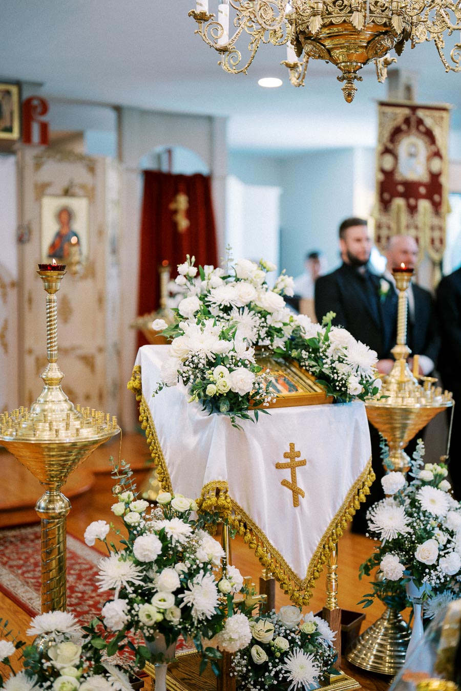 Ornate religious altar with white floral arrangements and gold accents in an Orthodox Christian church setting.