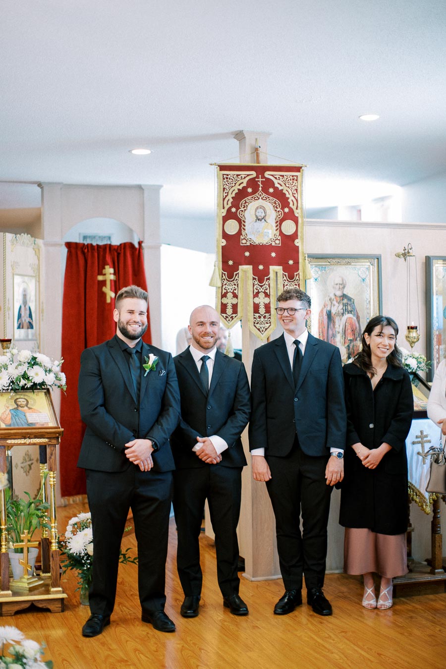 A group of four people in formal attire smiling inside an ornately decorated church, featuring religious icons and floral arrangements.