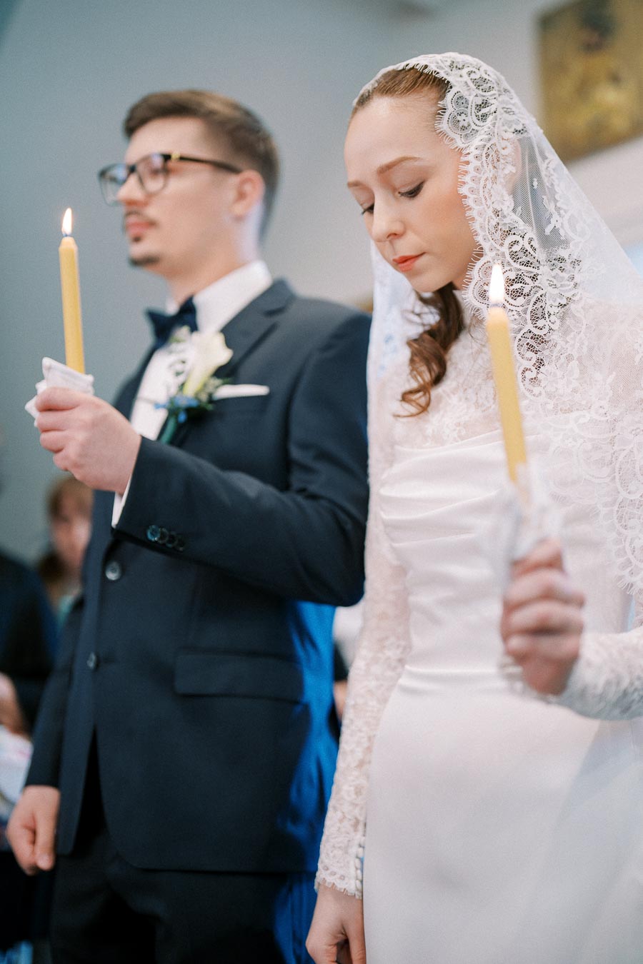 Bride and groom holding candles during a traditional wedding ceremony, dressed in elegant attire, bride wearing a lace veil.