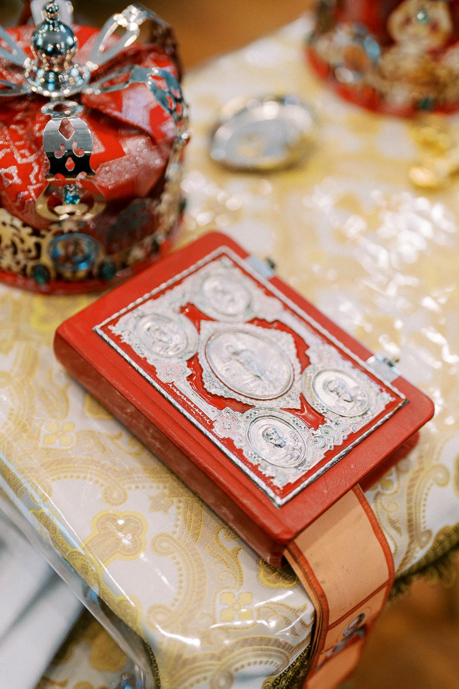 Ornate red religious book with silver detailing on a decorative table next to a red and gold ceremonial crown.