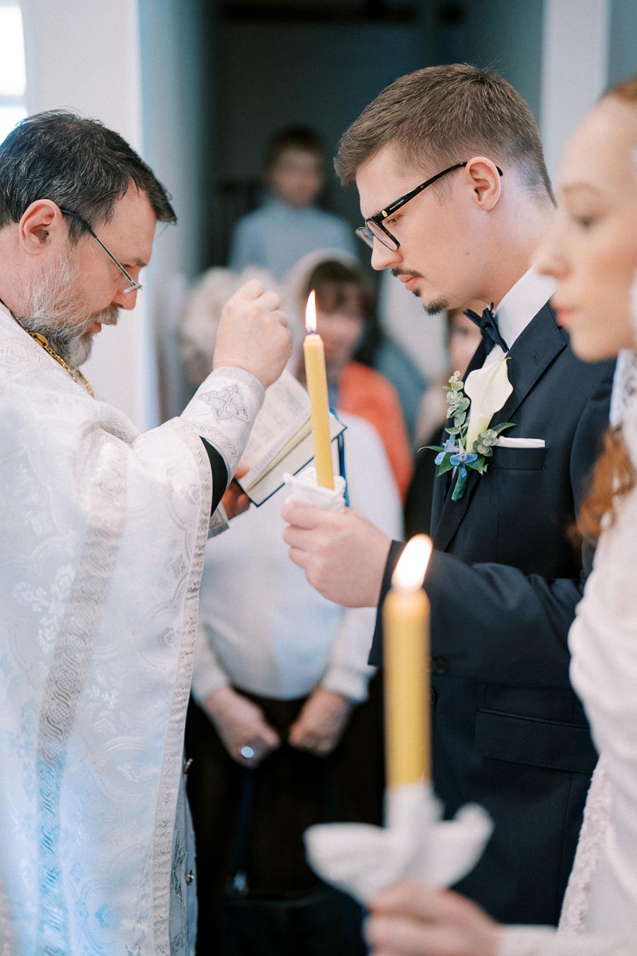 Priest blessing a couple holding candles during a wedding ceremony, with focus on traditional religious rituals and solemn atmosphere.