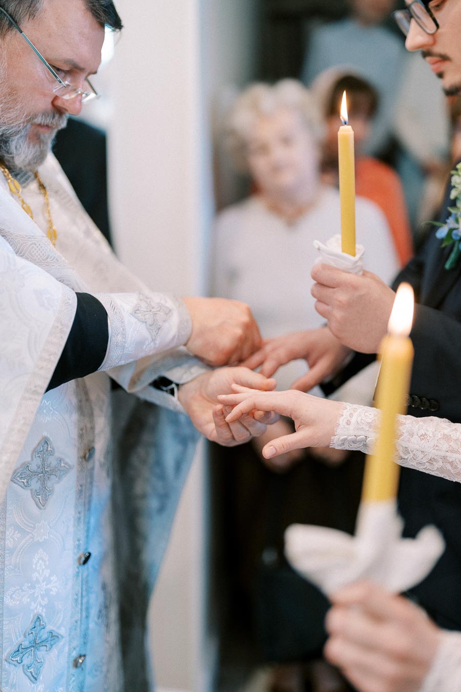 Priest conducting a traditional wedding ceremony, joining hands of bride and groom while they hold lit candles, symbolizing unity and faith.