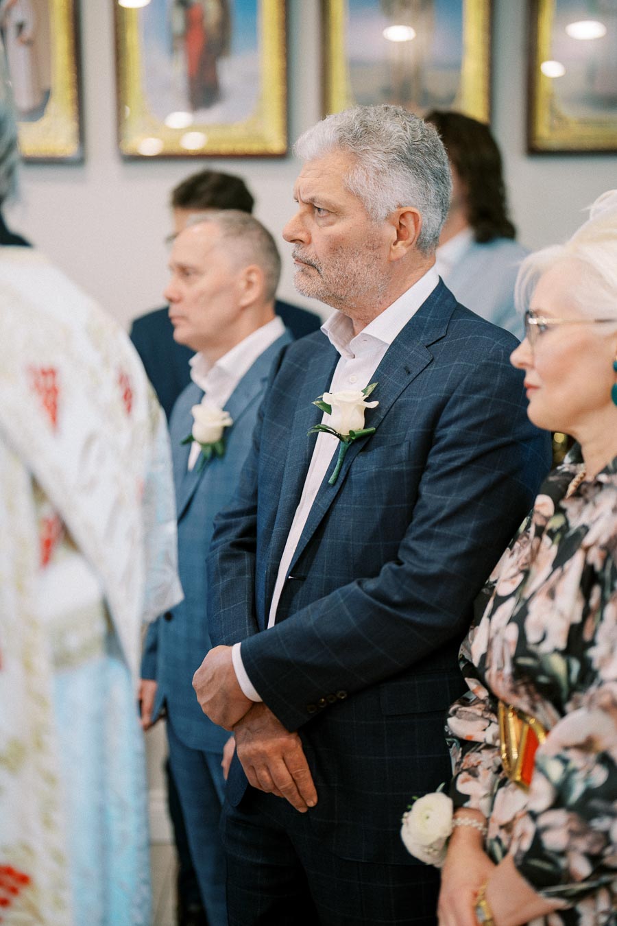 A group of formally dressed people attending a special ceremony, with a man in a blue suit holding a white rose and focusing on the event.