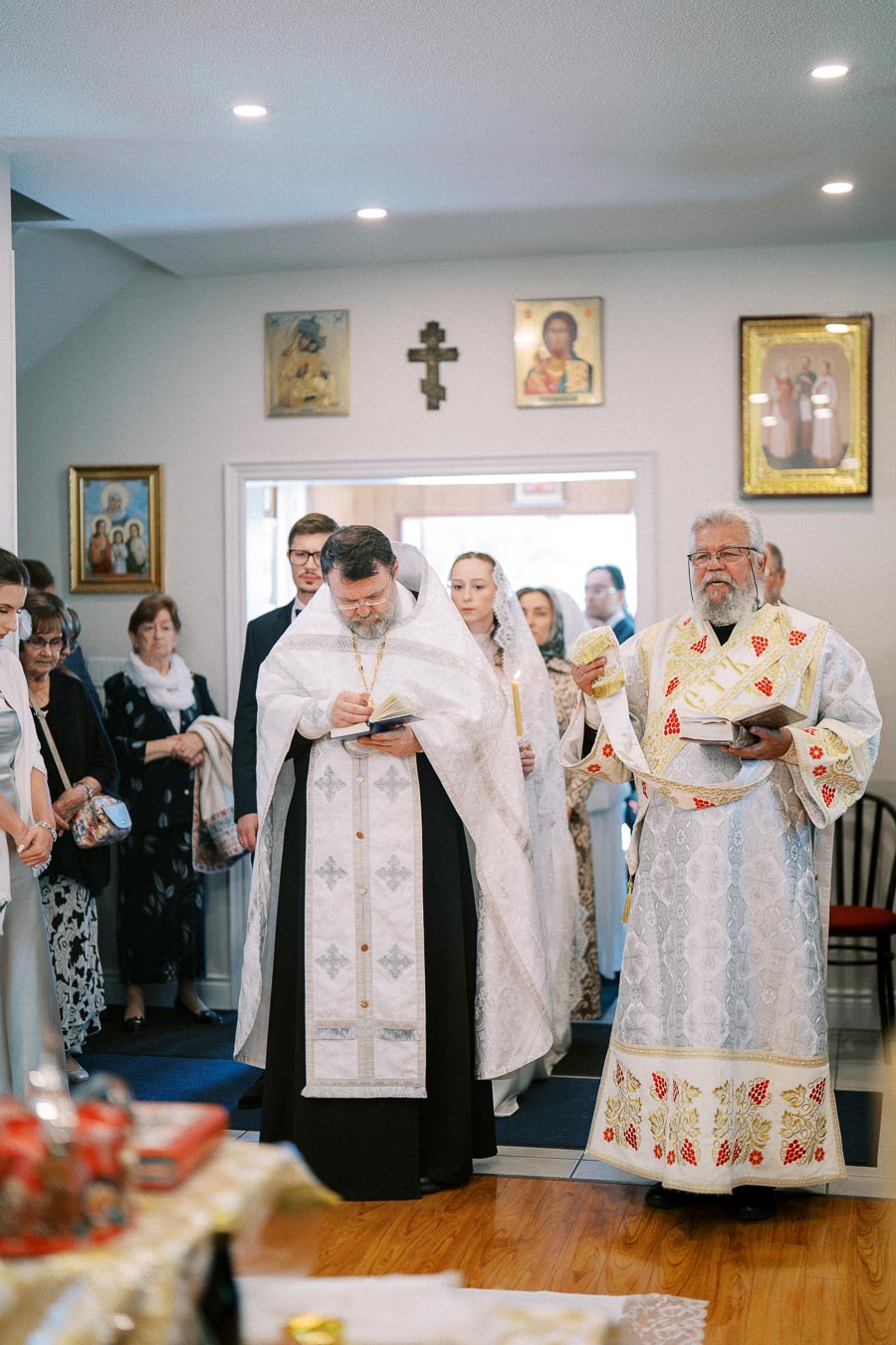 Priests conducting a religious ceremony in a decorated church with attendees observing in traditional attire, showcasing icons on the walls.