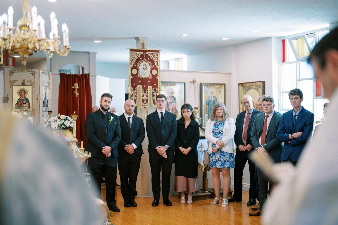 A group of people standing solemnly inside a church during a ceremony, with icons and religious decorations in the background.