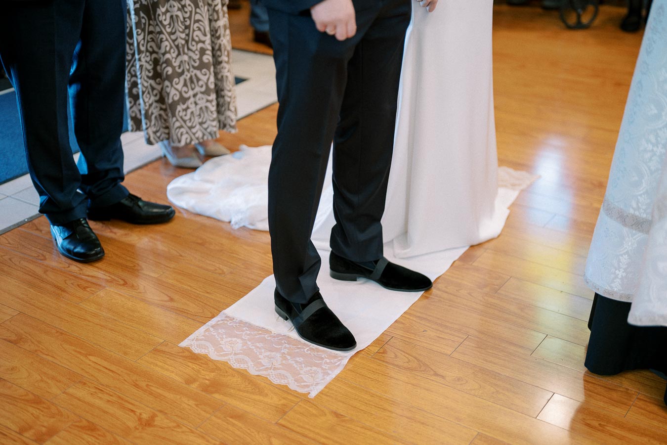 Wedding ceremony close-up of groom and bride standing on lace fabric, with focus on their shoes and floor.