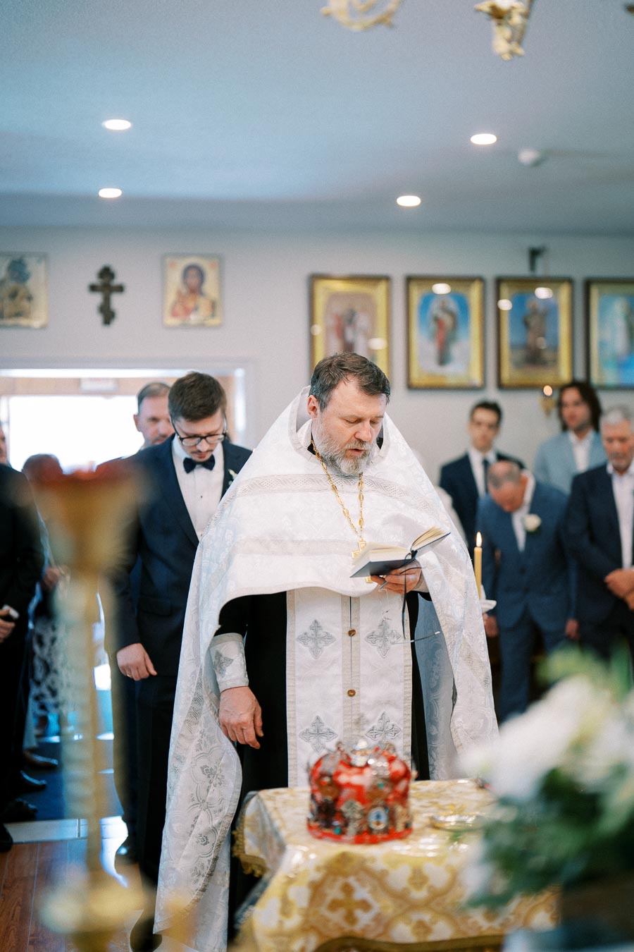 Priest conducting a traditional ceremony inside a church with followers, surrounded by religious icons and decor.