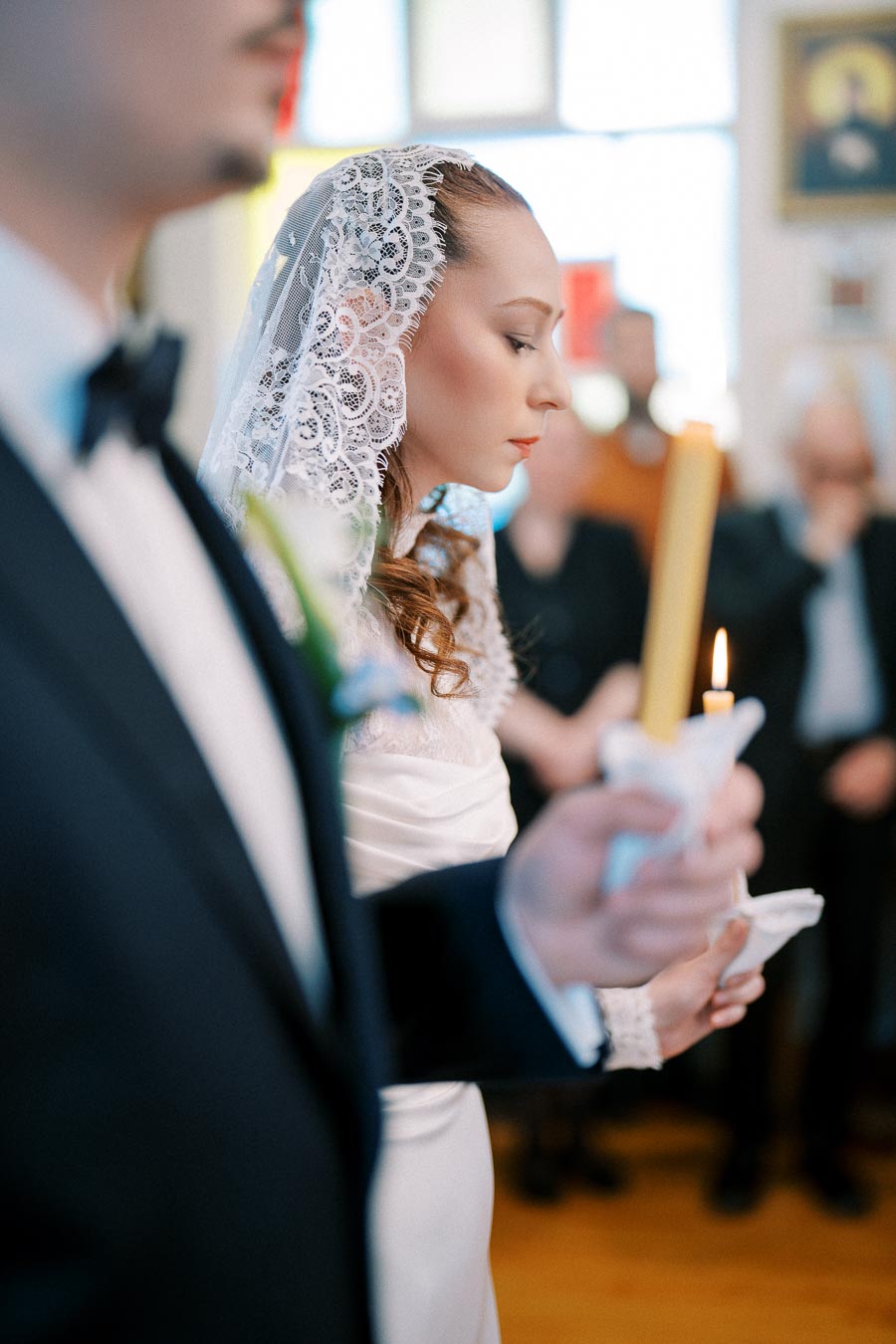 Bride and groom holding candles during a wedding ceremony, with the bride wearing a lace veil and focused expression.
