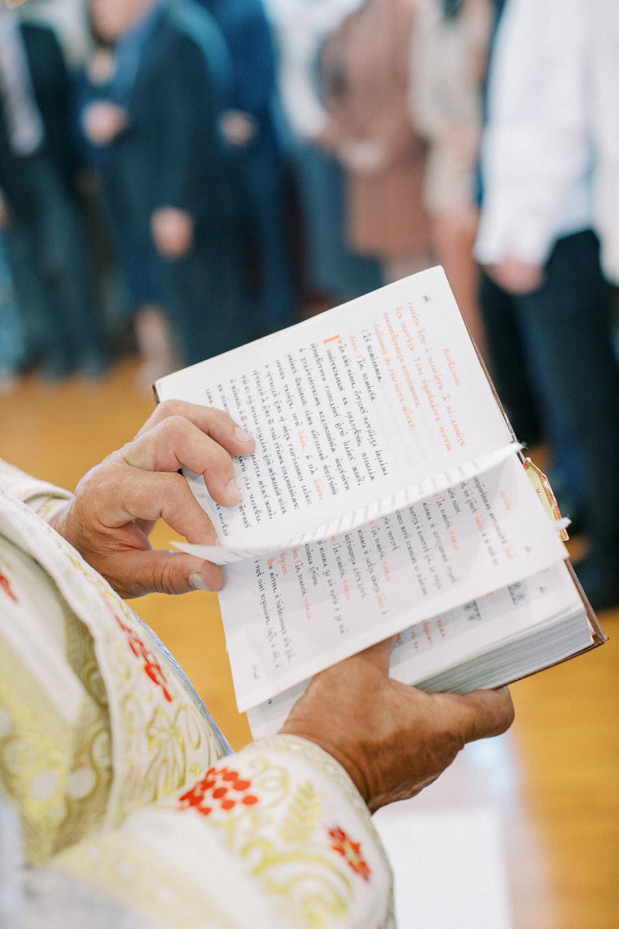 Close-up of a person in ornate traditional attire holding and turning the pages of a ceremonial book during a formal gathering.
