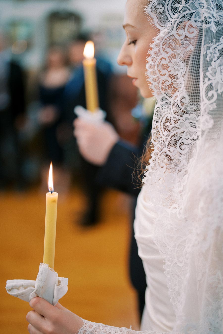 Bride in a lace veil holding a lit candle during a wedding ceremony.