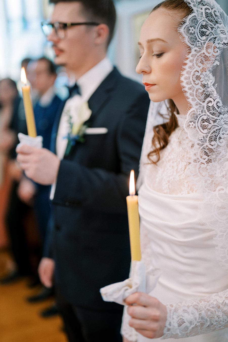 Bride and groom holding candles during wedding ceremony, with bride in lace veil and groom in formal suit