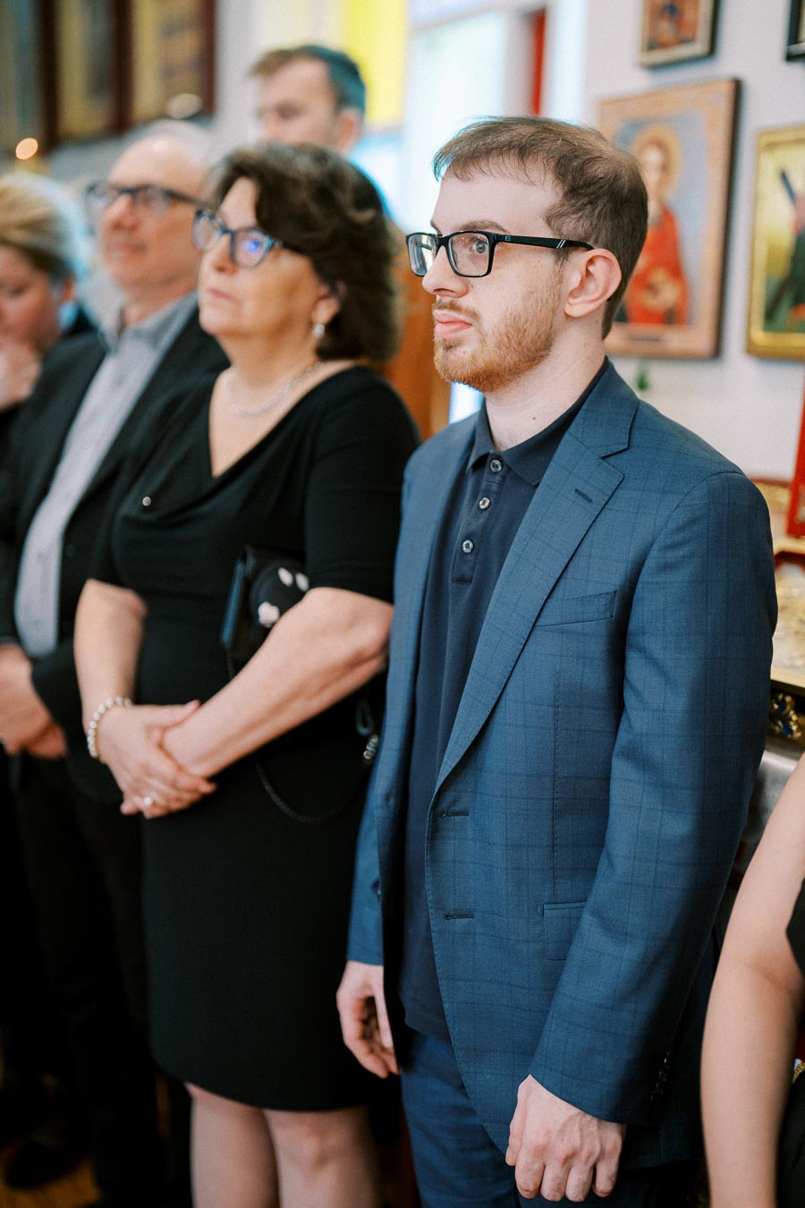 Group of people attentively attending an indoor event, with a man in a blue suit standing in focus in the foreground.