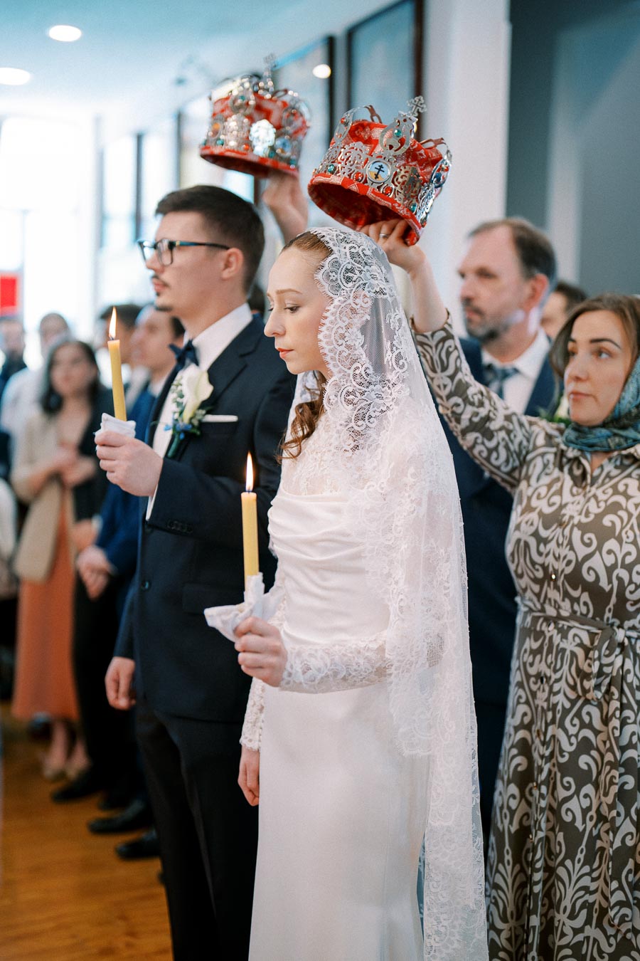 Orthodox wedding ceremony with bride and groom holding candles while ornate crowns are placed above their heads, symbolizing tradition and spiritual significance.