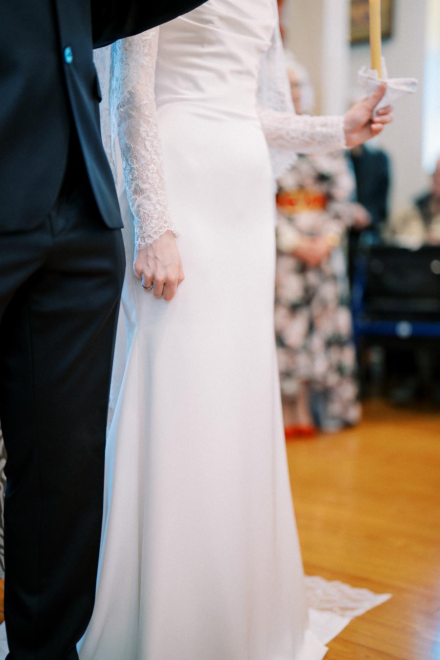 A bride and groom hold candles during their wedding ceremony, with the bride wearing an elegant white gown with lace sleeves.