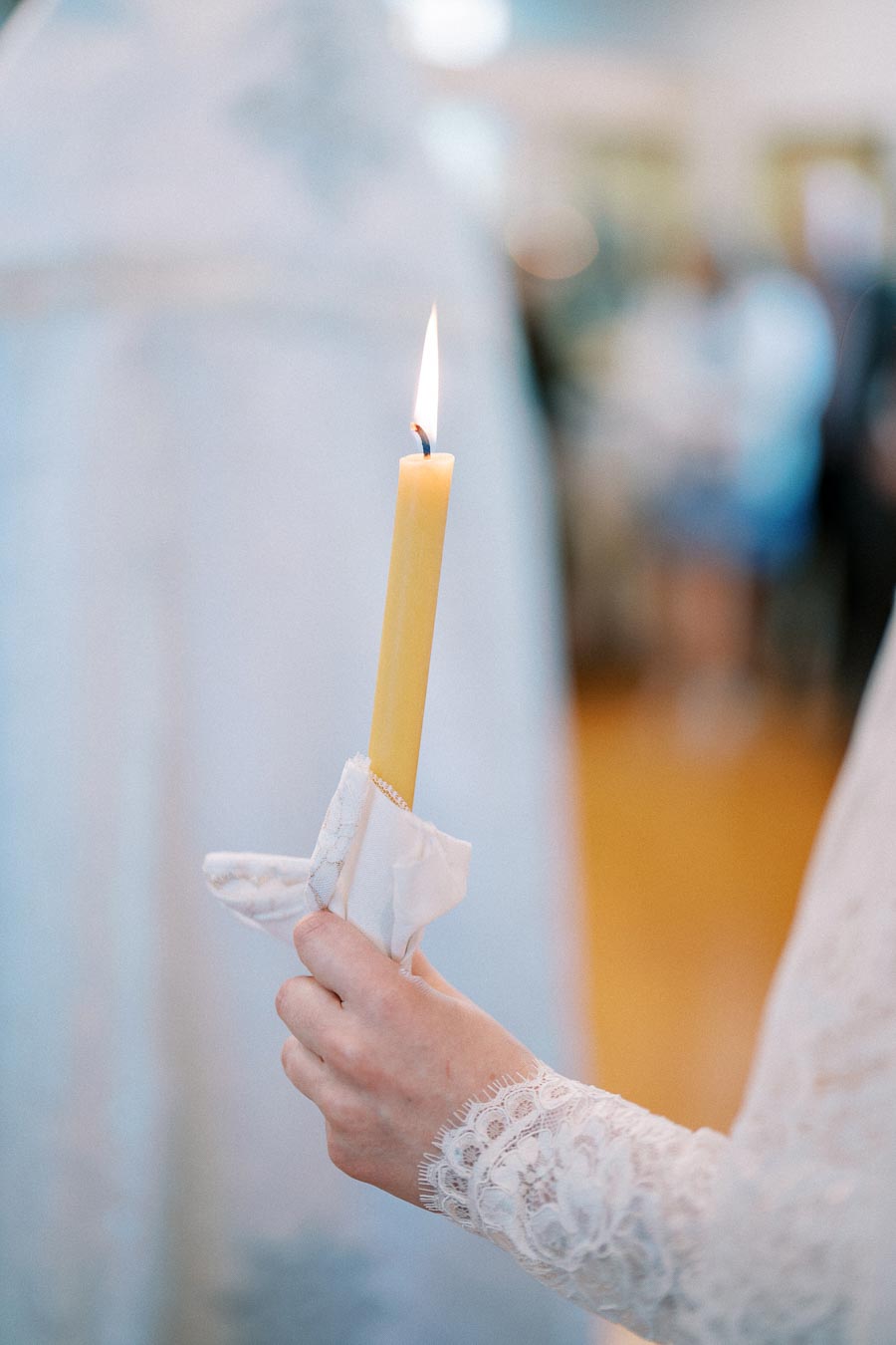 Hand holding a lit candle wrapped in lace cloth at a ceremonial event.