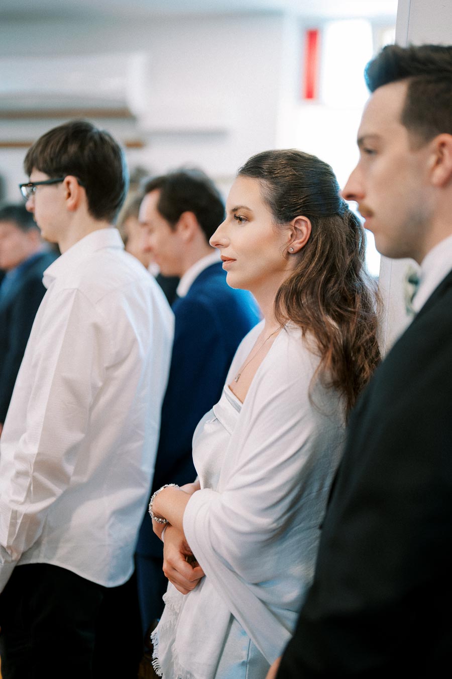 A group of people formally dressed, standing attentively during a ceremony in a bright room.