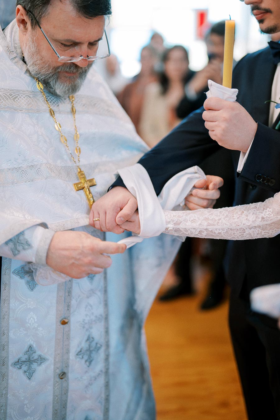 Priest officiating a traditional wedding ceremony, tying the hands of the bride and groom with a white sash, symbolizing unity and commitment in a religious setting.