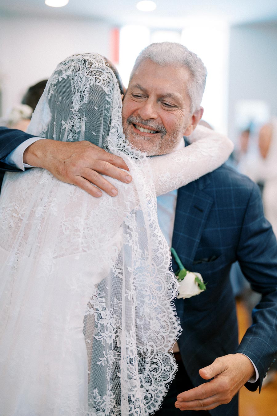 Father joyfully hugging bride in lace wedding dress during ceremony.