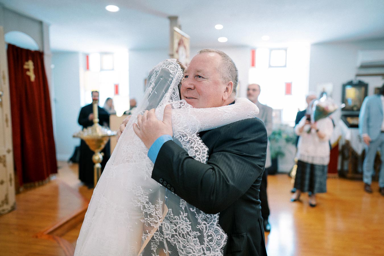 Emotional father-of-the-bride hug at wedding ceremony in church setting, highlighting familial love and celebration.