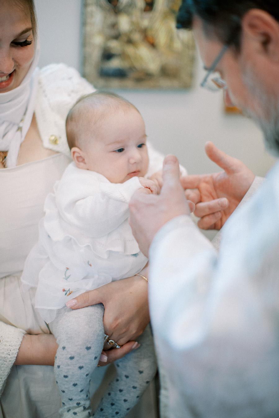 A baby being lovingly held during a baptism ceremony, surrounded by adults in a softly lit room, symbolizing family and tradition.