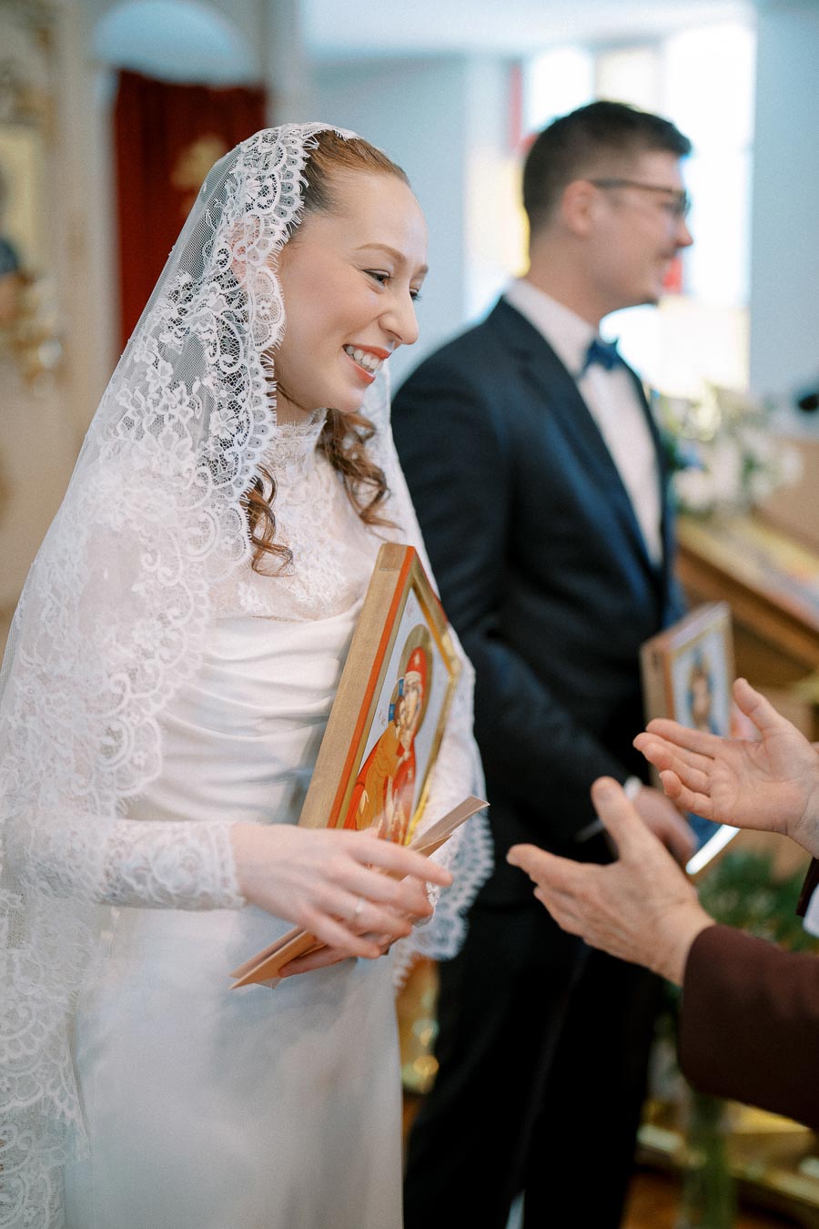 Bride in a lace veil holding a religious icon during a traditional wedding ceremony.