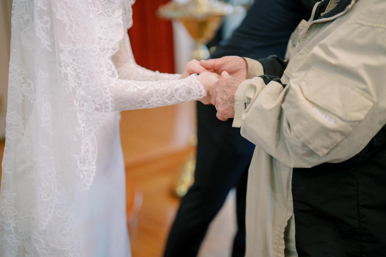 A bride in a lace wedding dress holds hands with an elderly person, symbolizing love and connection during a wedding ceremony.