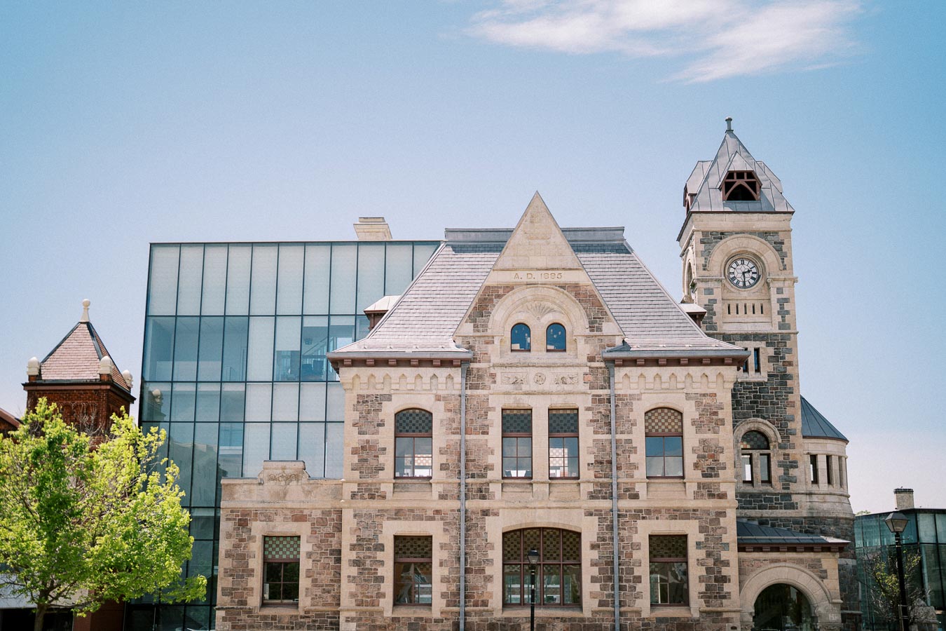 Historic building with clock tower, featuring stone architecture and modern glass extension, under a clear blue sky.