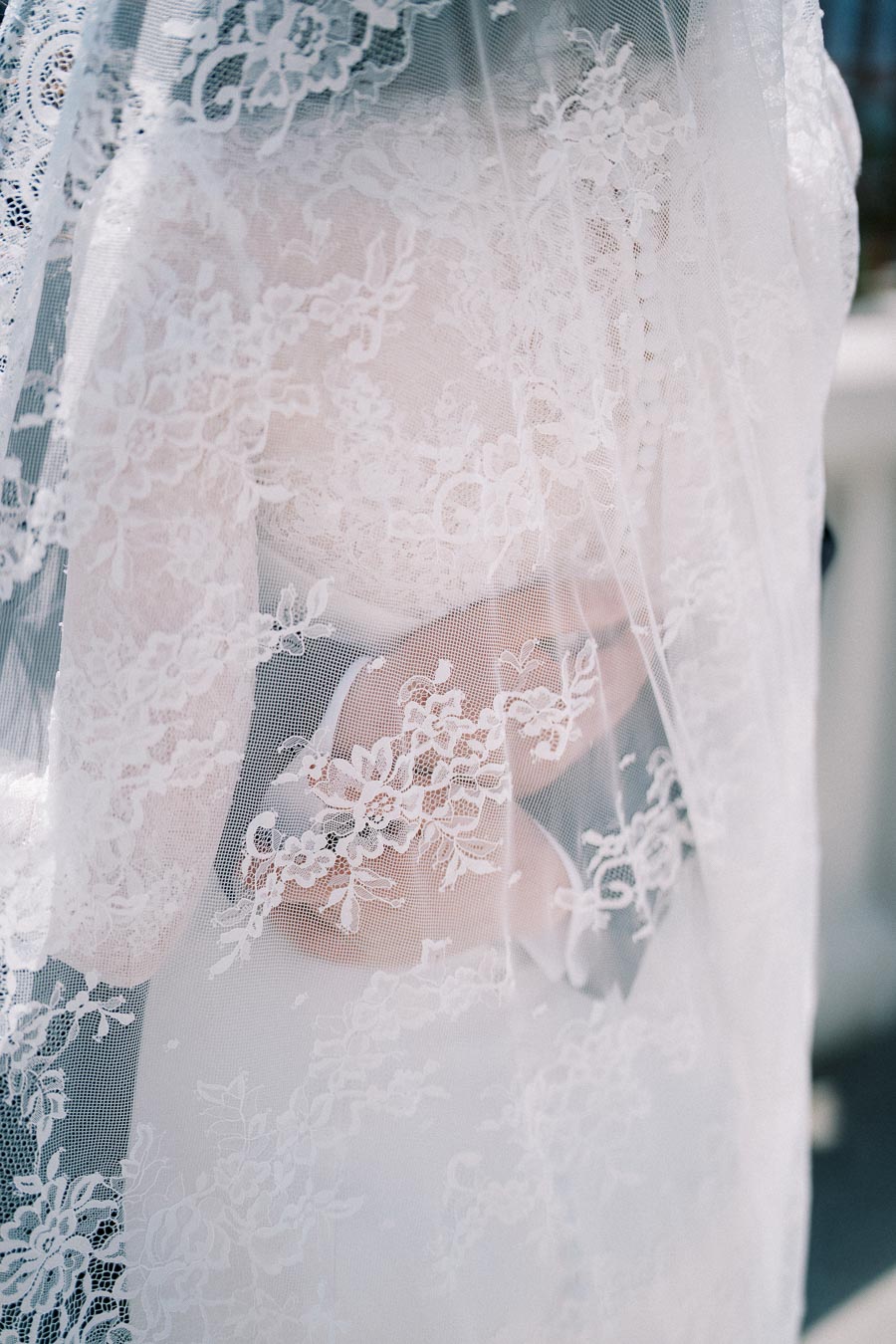 Bridal veil with intricate lace covering a wedding dress, capturing elegant patterns and delicate textures in soft natural light.