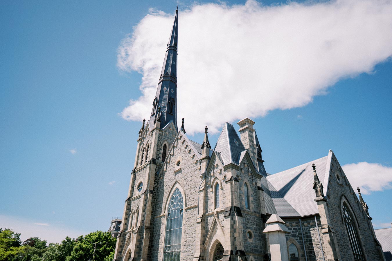 Gothic-style stone church with tall spire against a blue sky and white clouds.
