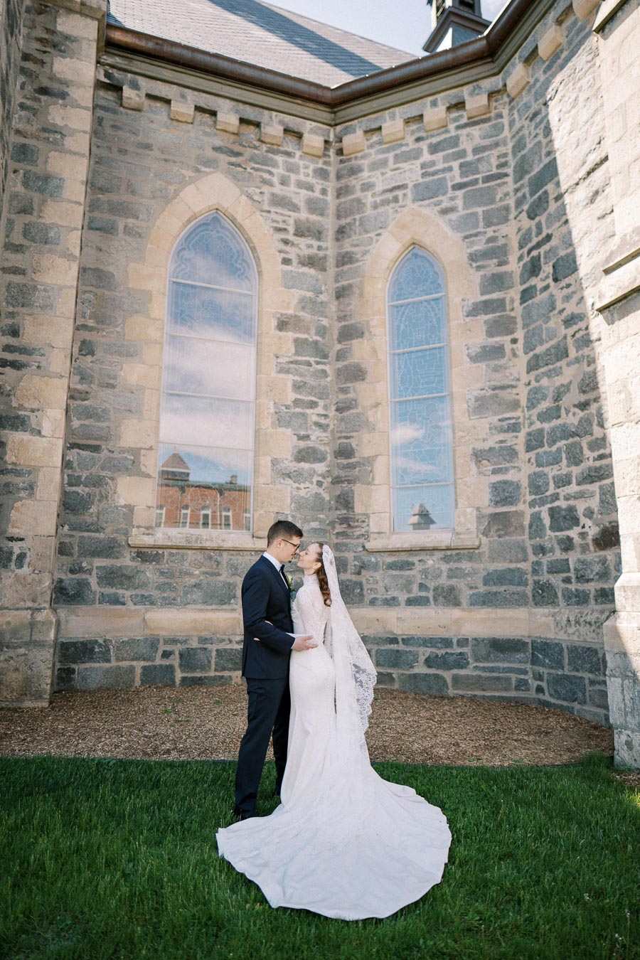 Bride and groom embracing in front of historic stone building with arched windows on their wedding day