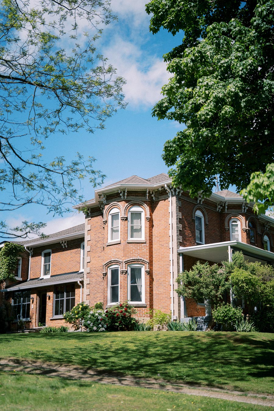 Elegant red brick Victorian-style house with lush greenery and blue sky.