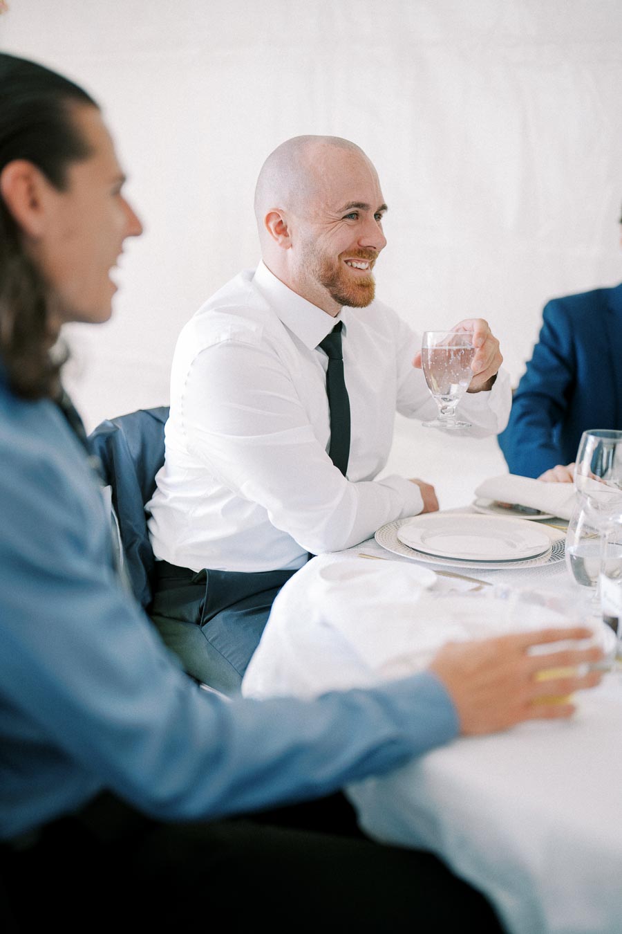 Man in white shirt and tie smiling while holding a glass at a formal dining event