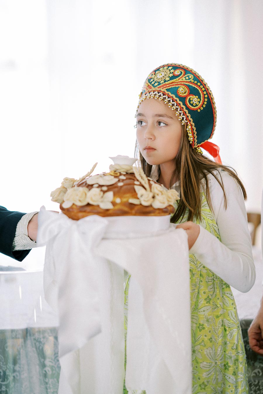 Young girl in traditional attire holding a decorated bread loaf during a cultural ceremony.