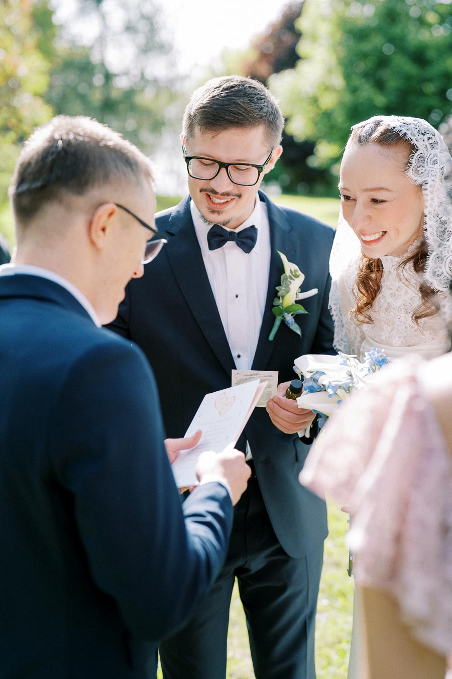 Smiling bride and groom during an outdoor wedding ceremony exchanging vows on a sunny day.