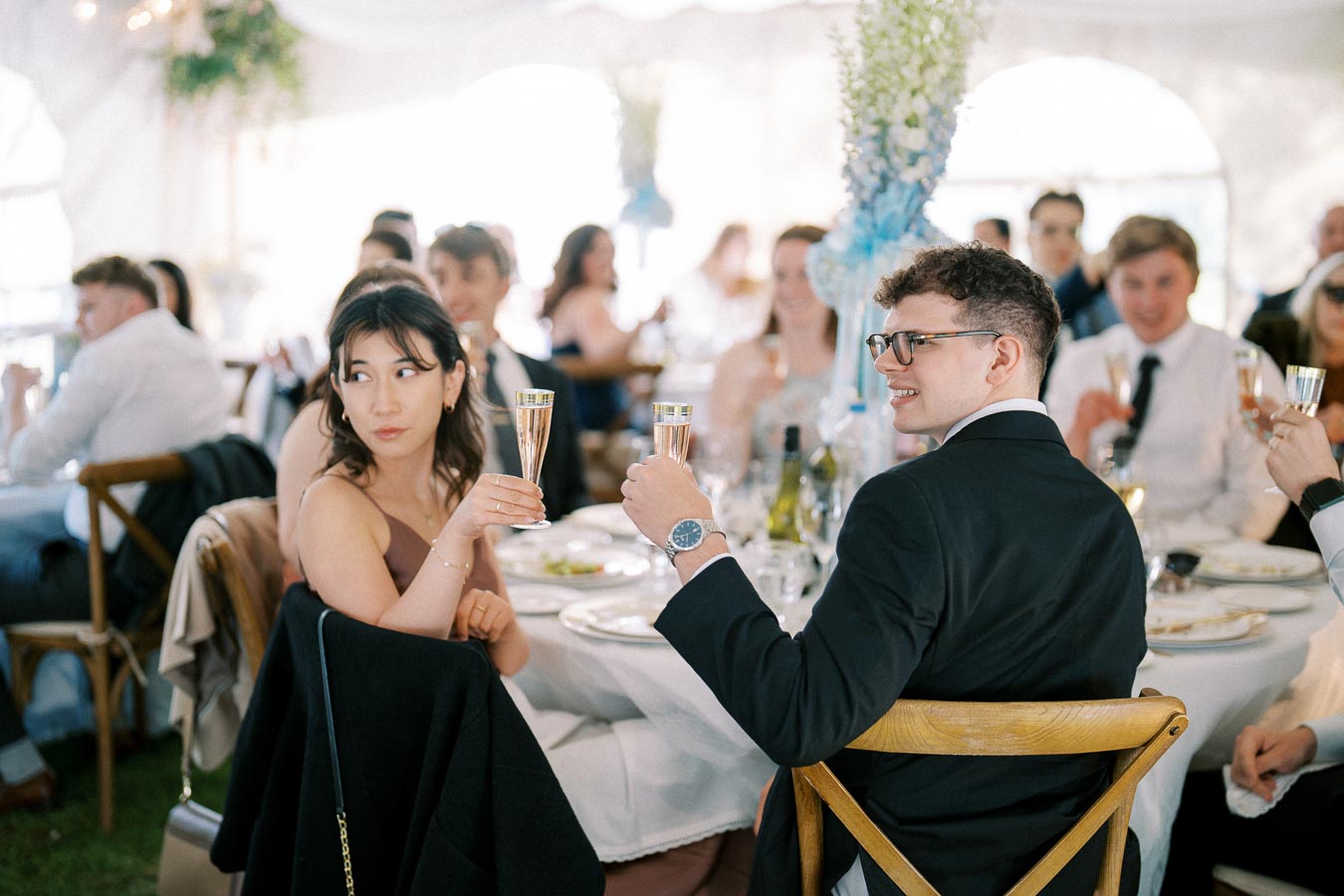 People raising champagne glasses at an elegant wedding reception, seated at a beautifully decorated banquet table with floral centerpieces.