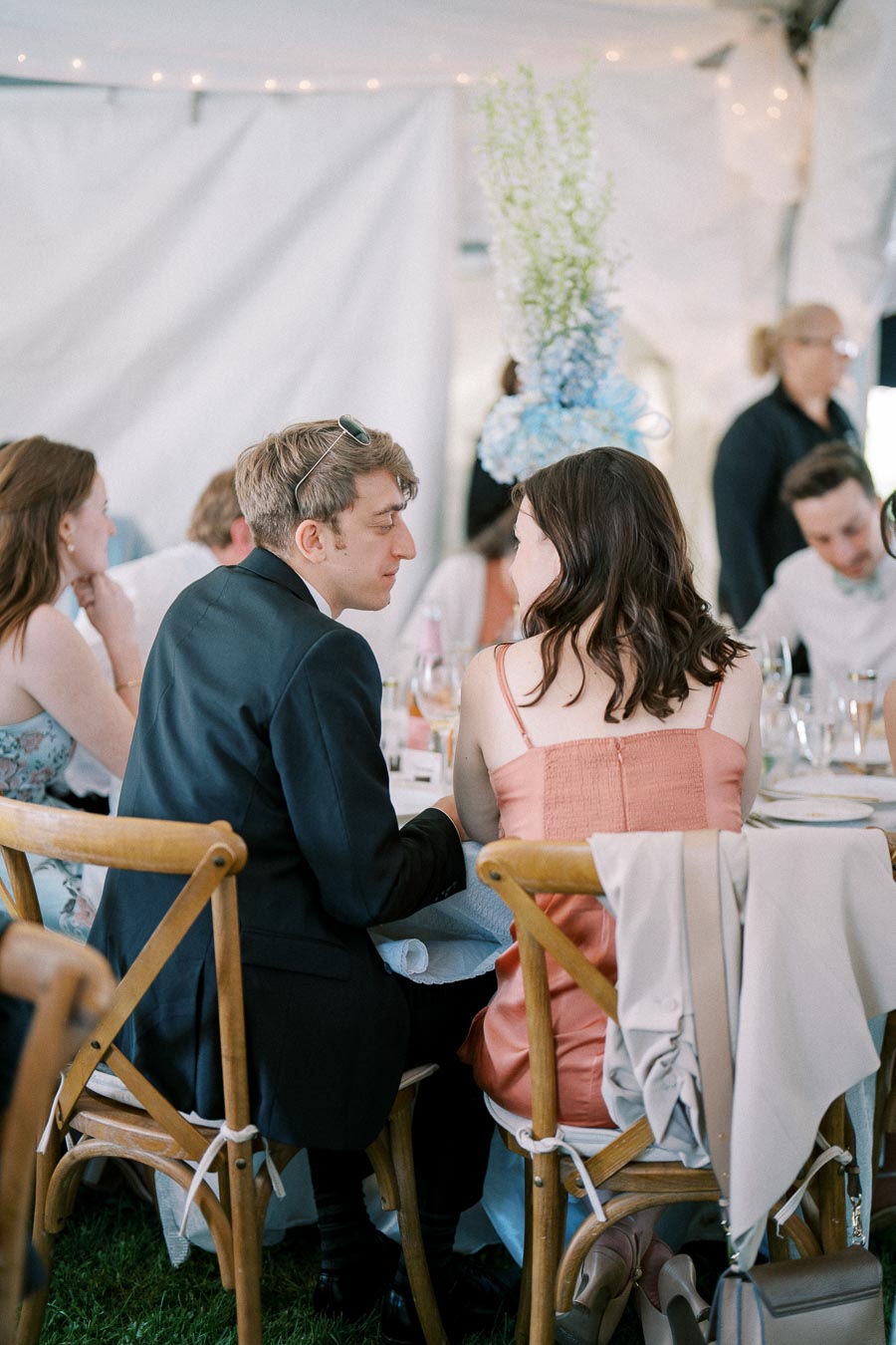 Guests seated at a stylish outdoor wedding reception, engaged in conversation, with elegant table decor and ambient lighting in the background.
