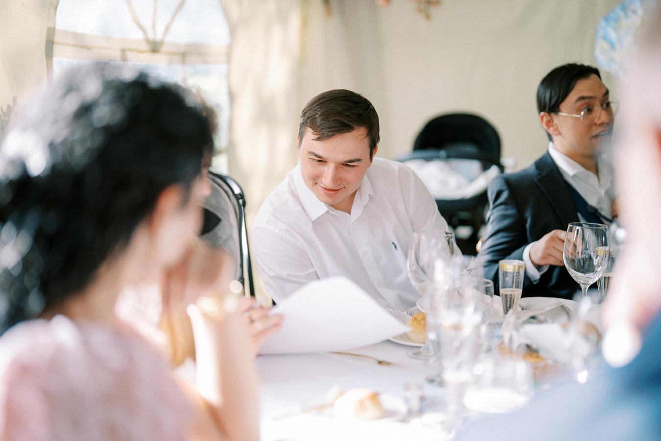 Group of people enjoying a conversation at a formal dining table event, sharing papers and surrounded by elegant glassware and table settings.