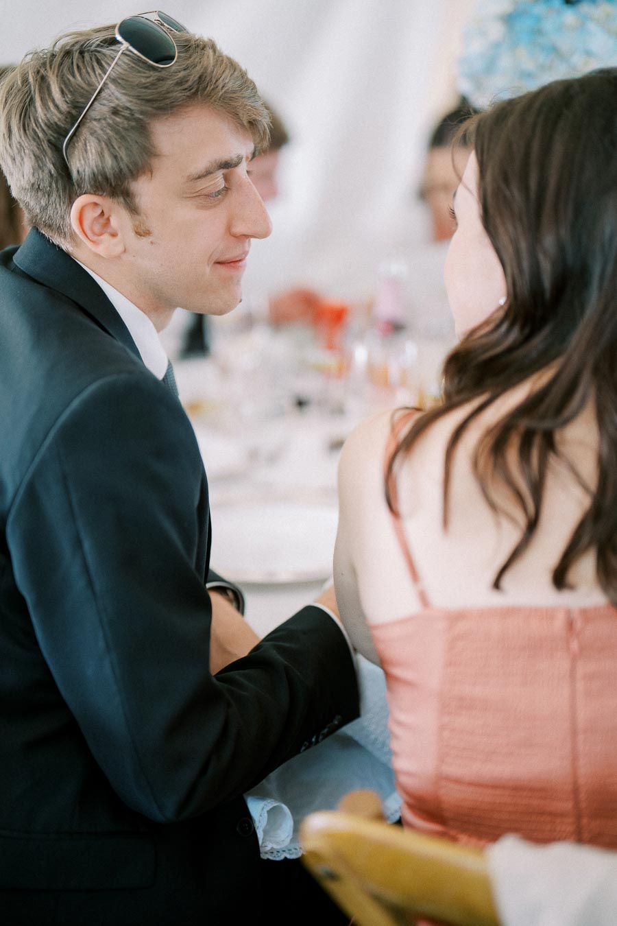 A young man in a suit with sunglasses on his head smiling at a woman in a pink dress at a formal event.